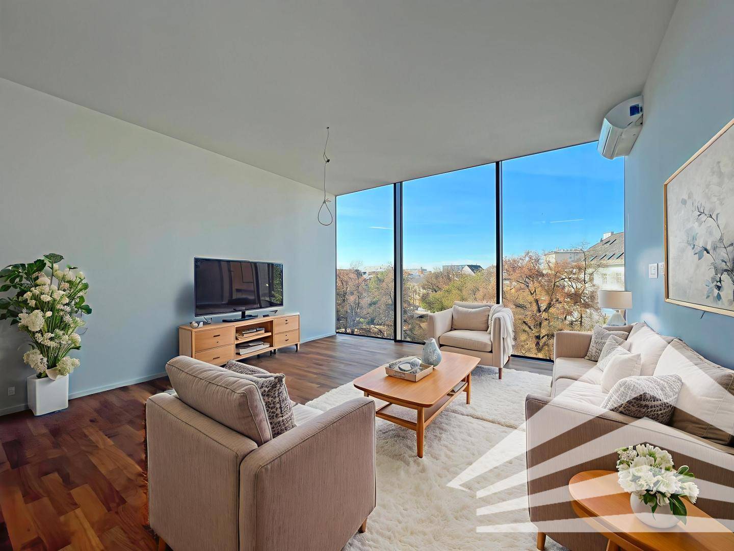 Gemütliches Wohnzimmer mit Holzboden, bequemen Sofas und Blick auf Bäume und Stadt.
