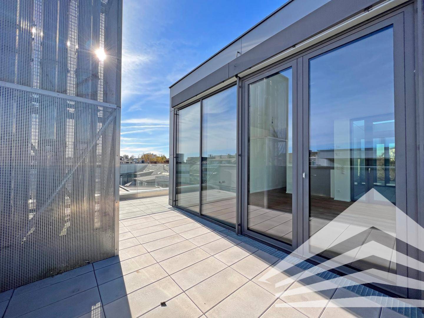 Sonnige Dachterrasse mit Fliesenboden und modernen Glasfronten, die viel Licht hereinlassen.