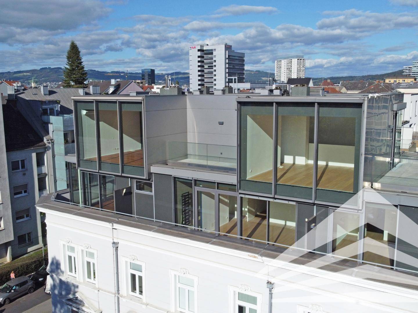 Moderne Dachaufbauten mit großen Glasflächen auf einem historischen Gebäude in städtischer Umgebung.