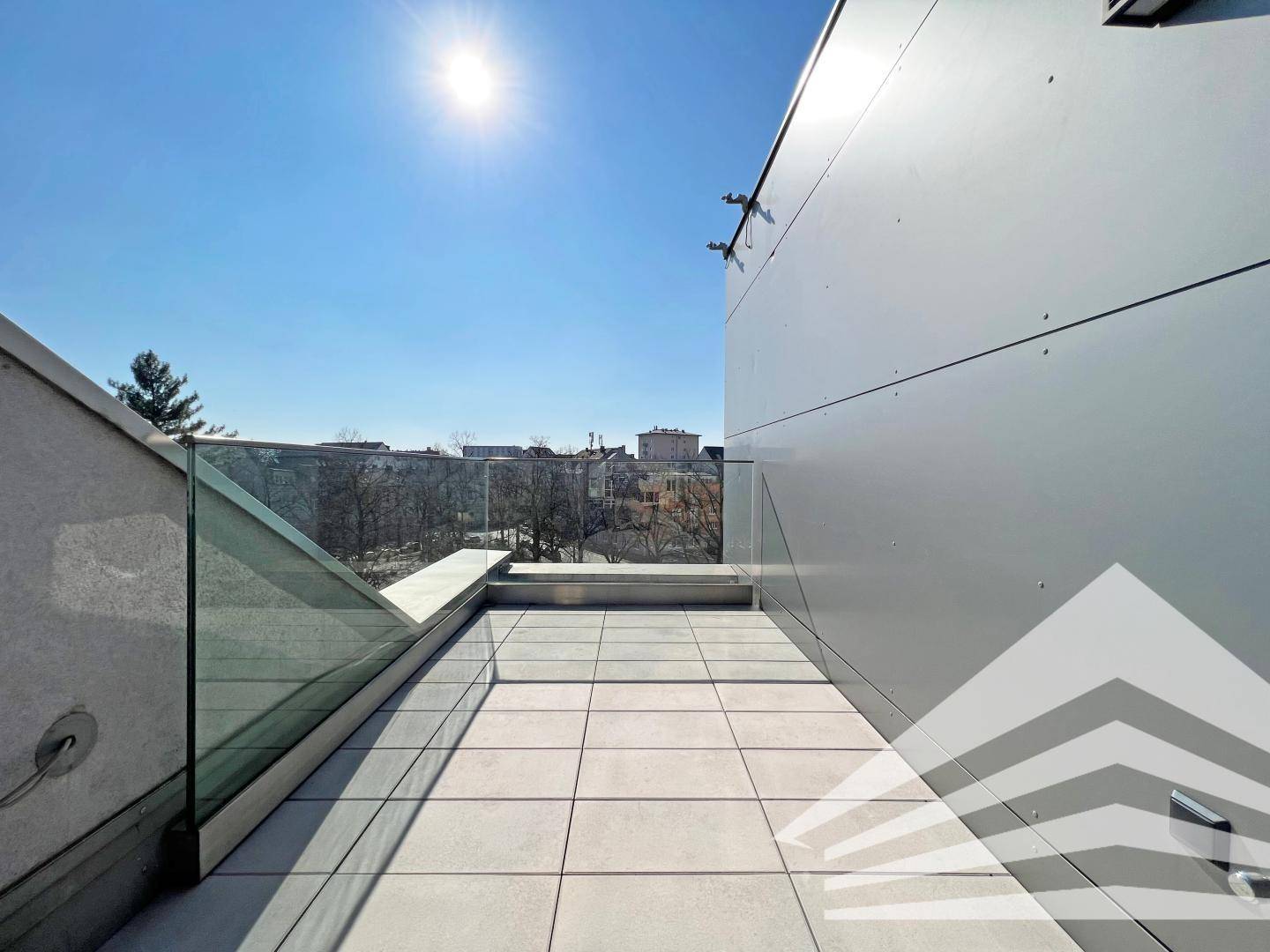 Sonnige Dachterrasse mit Fliesenboden und Glasgeländer, bietet einen weiten Blick über die Stadt.