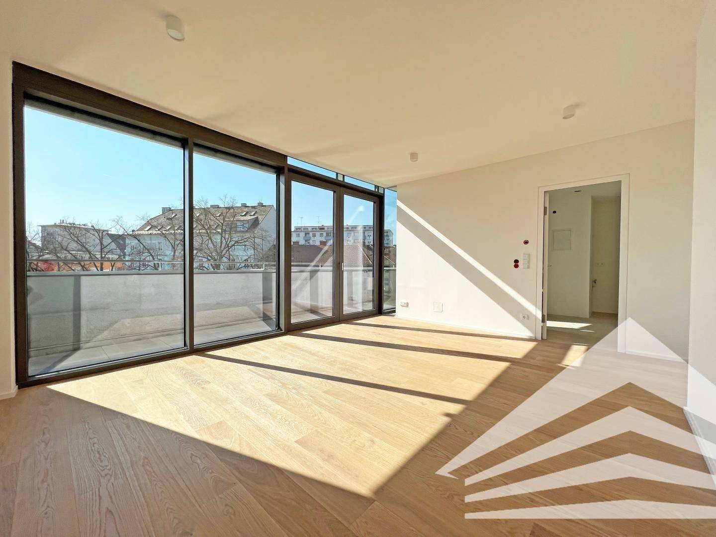 Lichtdurchfluteter Wohnbereich mit Holzboden und Zugang zu einem Balkon, bietet viel Sonnenlicht.