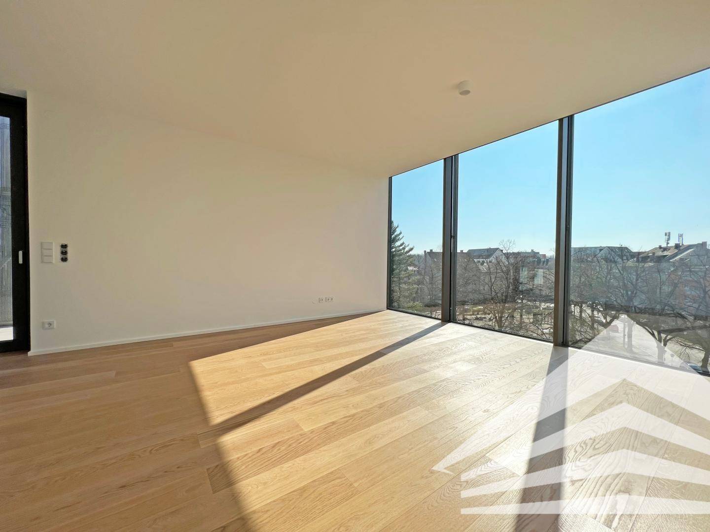 Heller, leerer Raum mit großen bodentiefen Fenstern und Holzboden, ideal für ein Wohnzimmer.