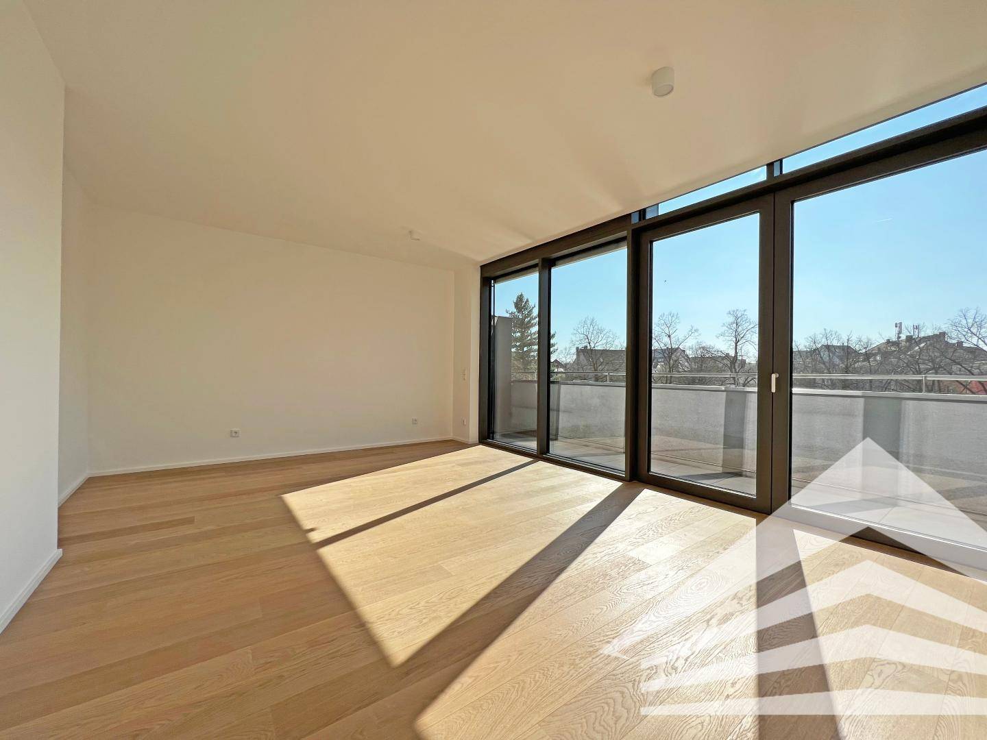 Geräumiger, heller Raum mit Holzboden und bodentiefen Fenstern, die viel Tageslicht hereinlassen.