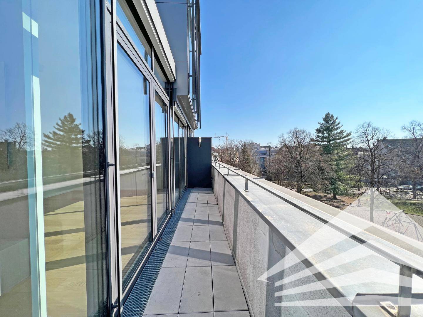 Langer, schmaler Balkon mit Fliesenboden und Glasgeländer, bietet einen Blick auf die Umgebung.
