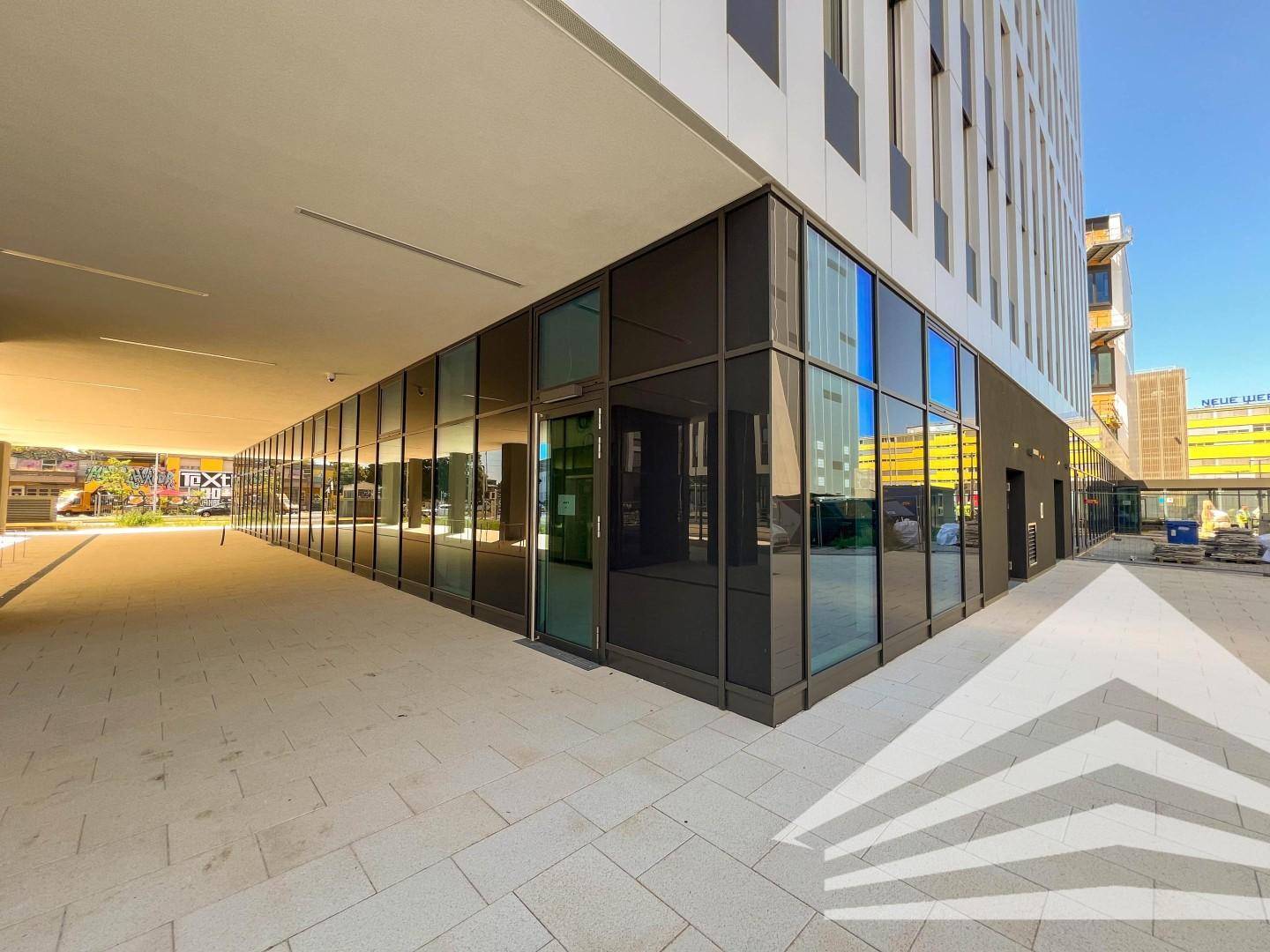 Moderner Eingangsbereich mit großen Glasfronten und einem überdachten Gehweg, der viel natürliches Licht hereinlässt.