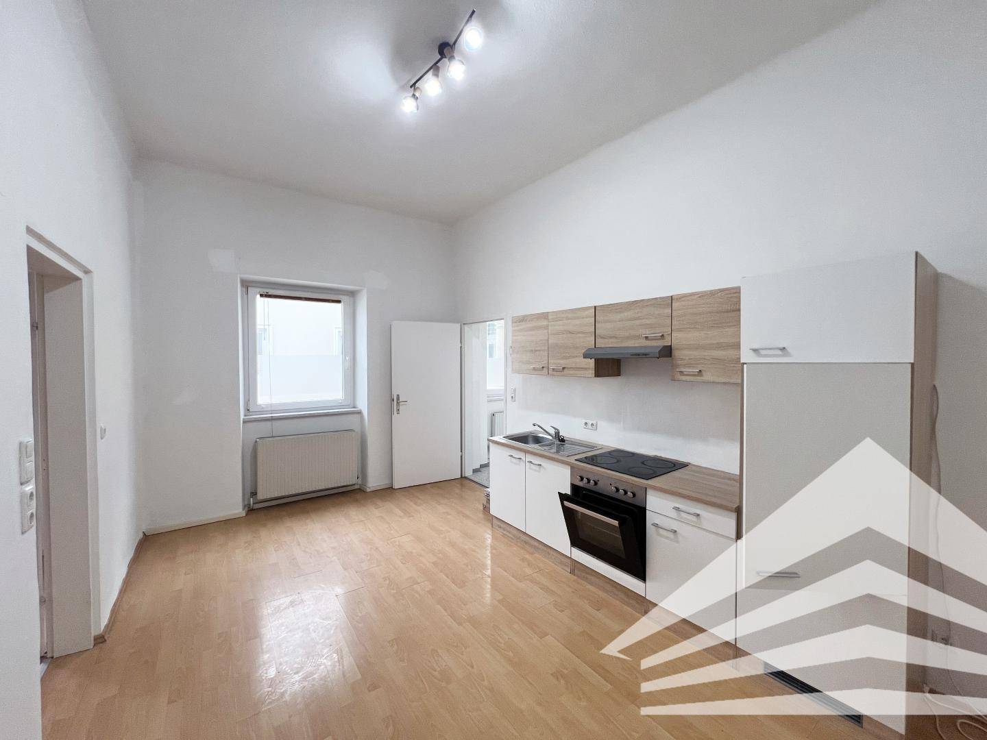 Kompakte Küchenzeile mit Fenster und hellem Parkettboden, ideal für kleine Wohnungen.