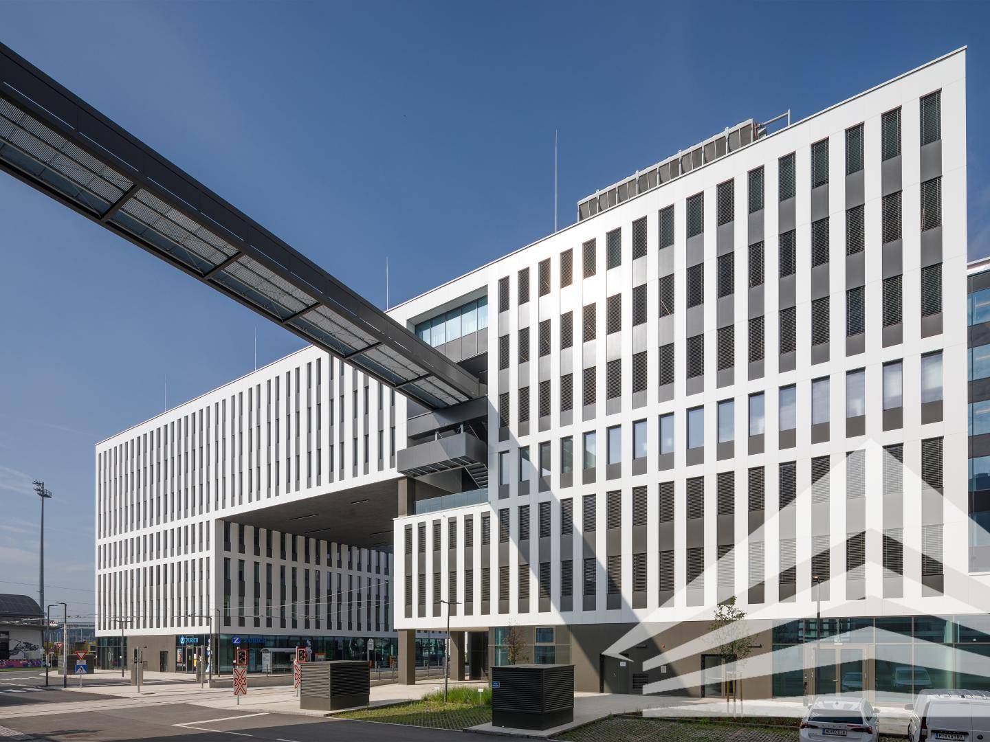 Moderner Bürokomplex mit markanter Architektur, Verbindungsbrücke und klarem Himmel.