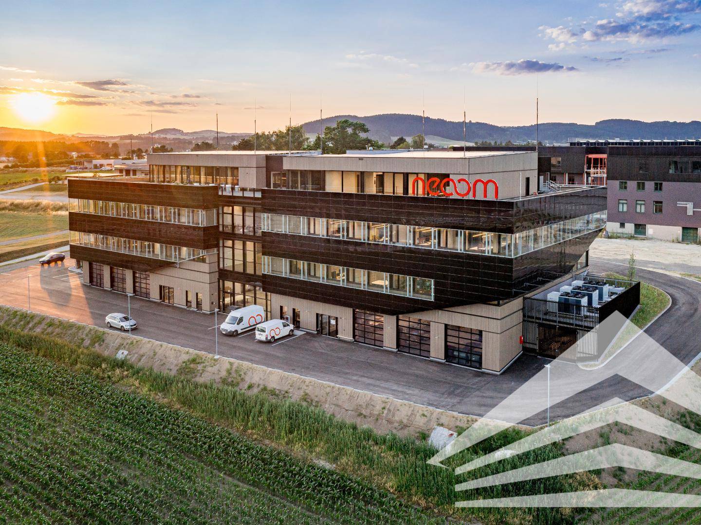 Modernes Bürogebäude mit Glasfassade und Holzverkleidung, umgeben von grüner Landschaft bei Sonnenuntergang.