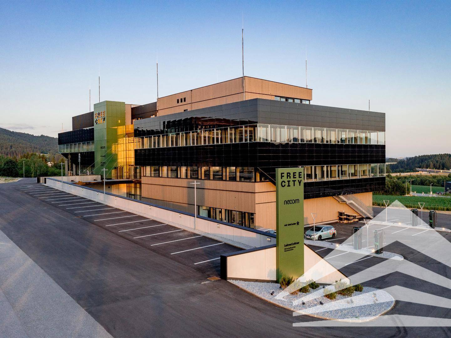 Modernes Bürogebäude mit markanter Architektur, großen Glasflächen und Beschilderung bei Sonnenuntergang.