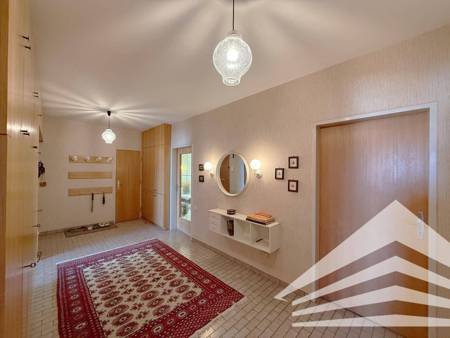 Heller Eingangsbereich mit Fliesenboden, Garderobe und dekorativem Spiegel.
