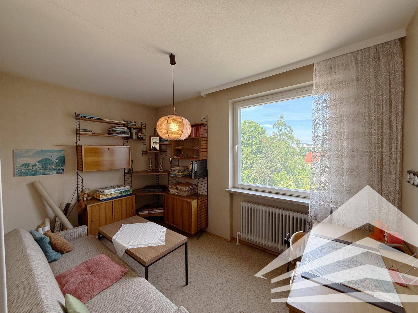 Gemütlicher Wohnraum mit Teppichboden, Regalsystem und großem Fenster.