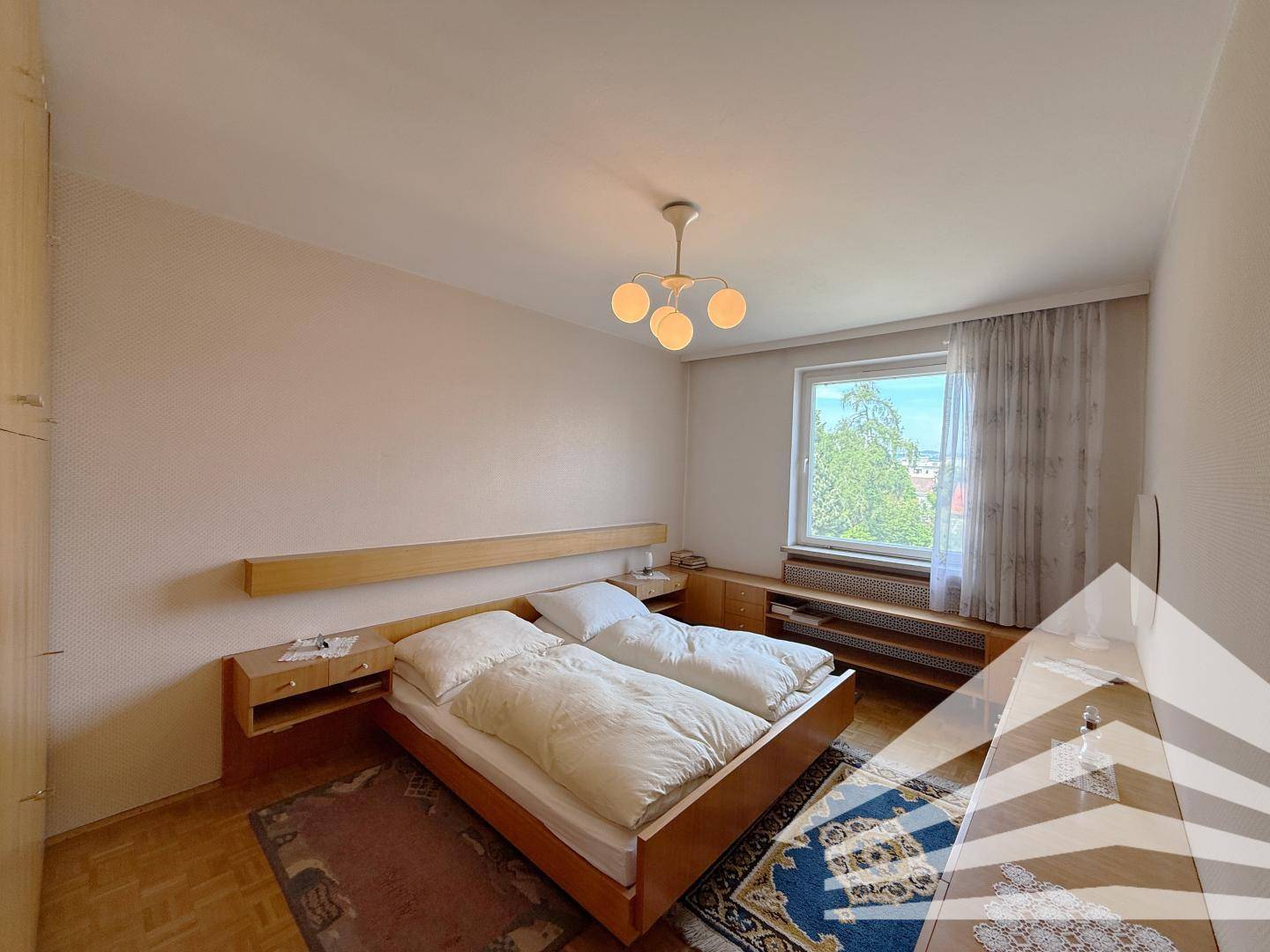 Schlafzimmer mit Parkettboden, Doppelbett und großem Fenster mit Blick ins Grüne.