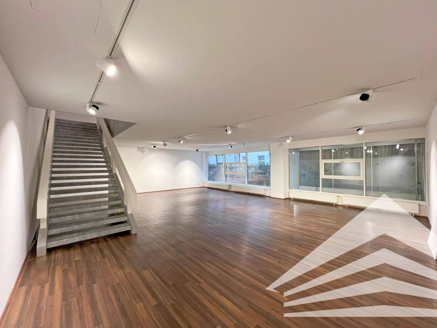 Offener Gewerberaum mit breiter Treppe und großen Fenstern, ideal für eine ansprechende Präsentation.