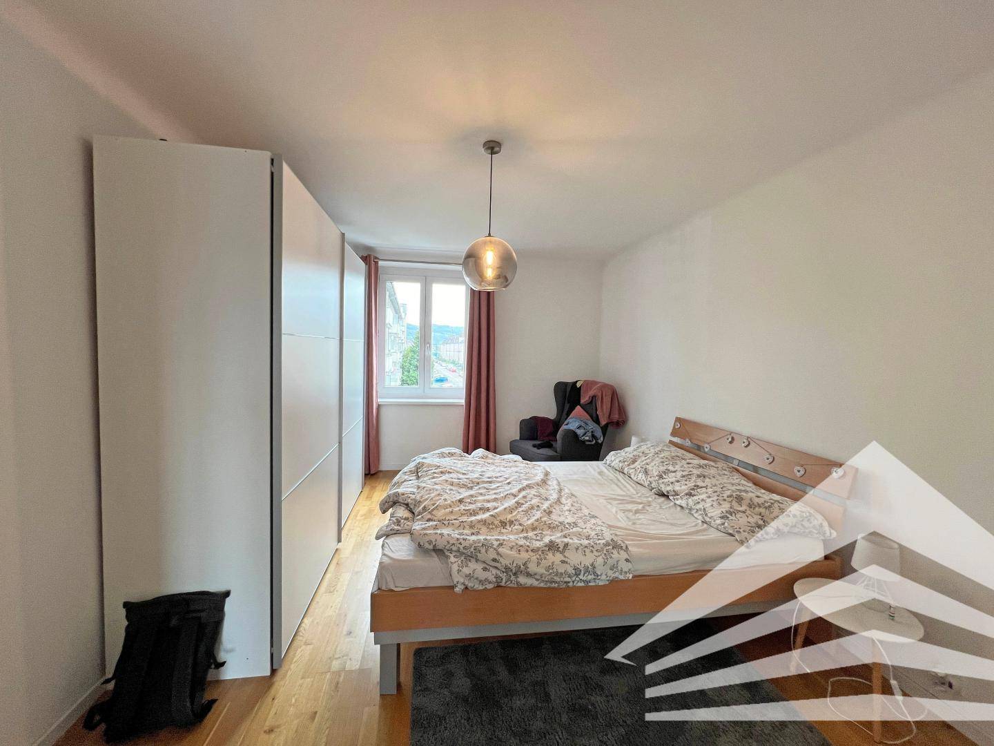 Schlafzimmer mit Holzbett, großem Kleiderschrank und Parkettboden, hell und funktional eingerichtet.