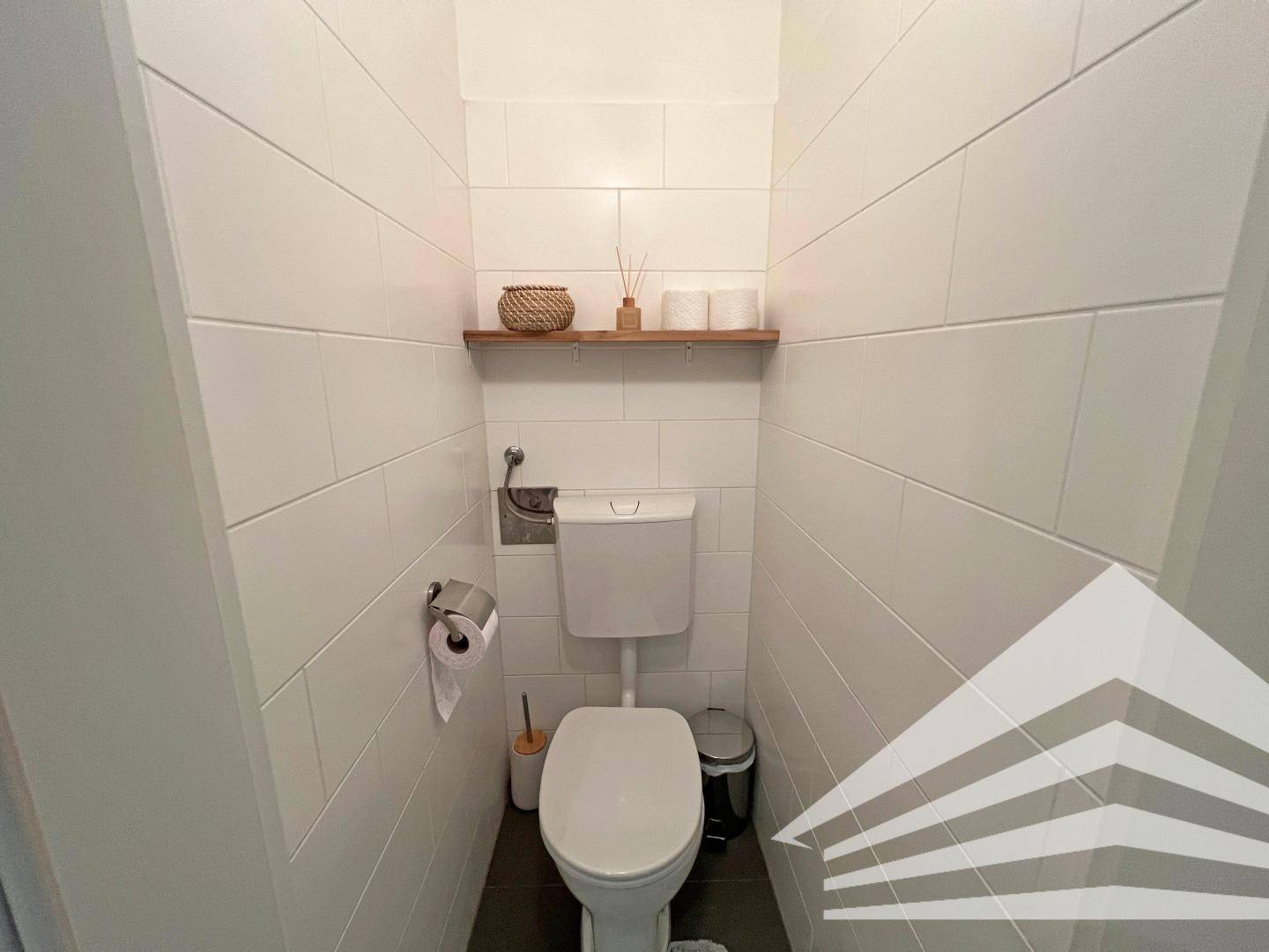 Separates WC mit Wand-WC und Regal, komplett gefliest in Weiß.