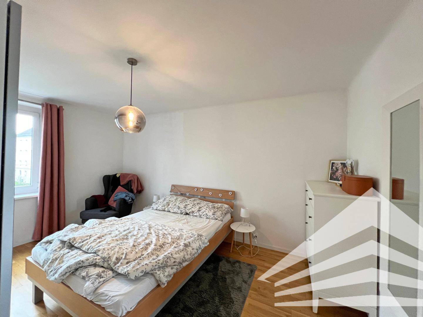 Helles Schlafzimmer mit Holzbett, Nachttisch und Kommode, ausgestattet mit Parkettboden.
