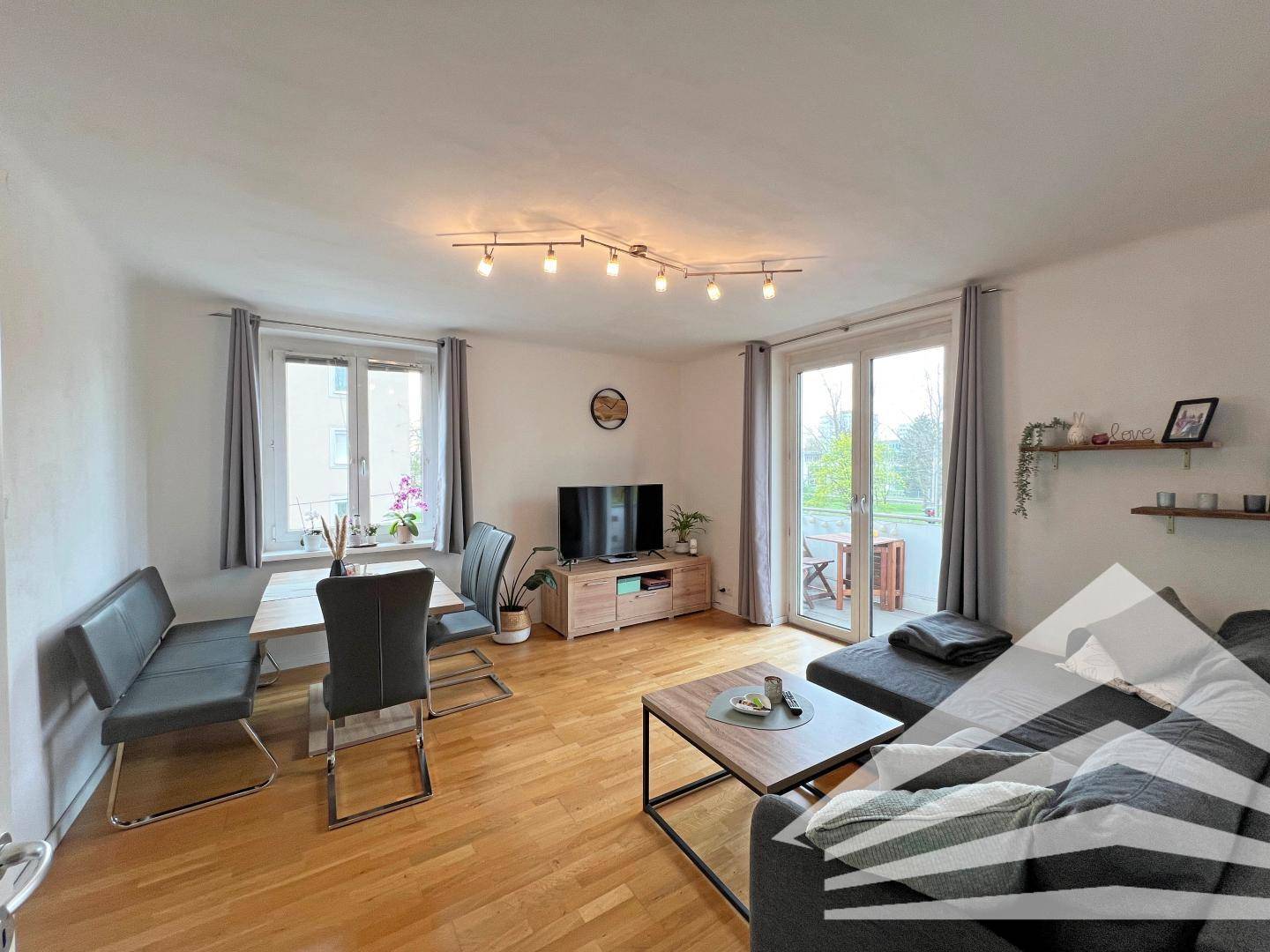 Geräumiger Wohn- und Essbereich mit Parkettboden, Sofa und Esstisch, mit Balkonzugang.