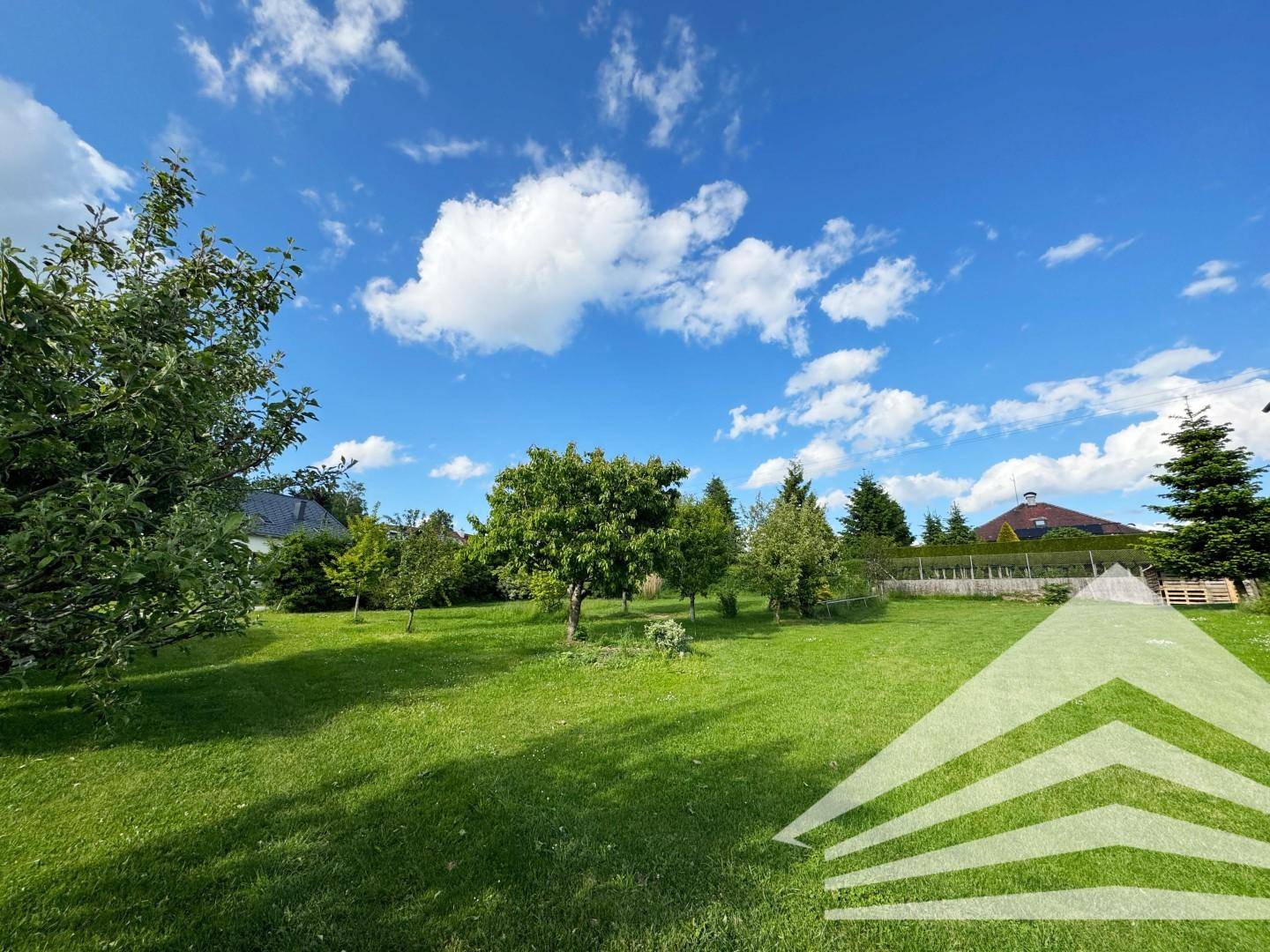 Idyllische Gartenlandschaft mit gepflegtem Rasen und schattenspendenden Bäumen an einem sonnigen Tag.
