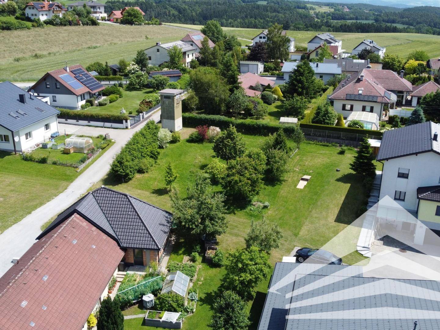 Weitläufige Luftaufnahme eines Wohngebiets mit viel Grün und Blick auf die hügelige Landschaft.