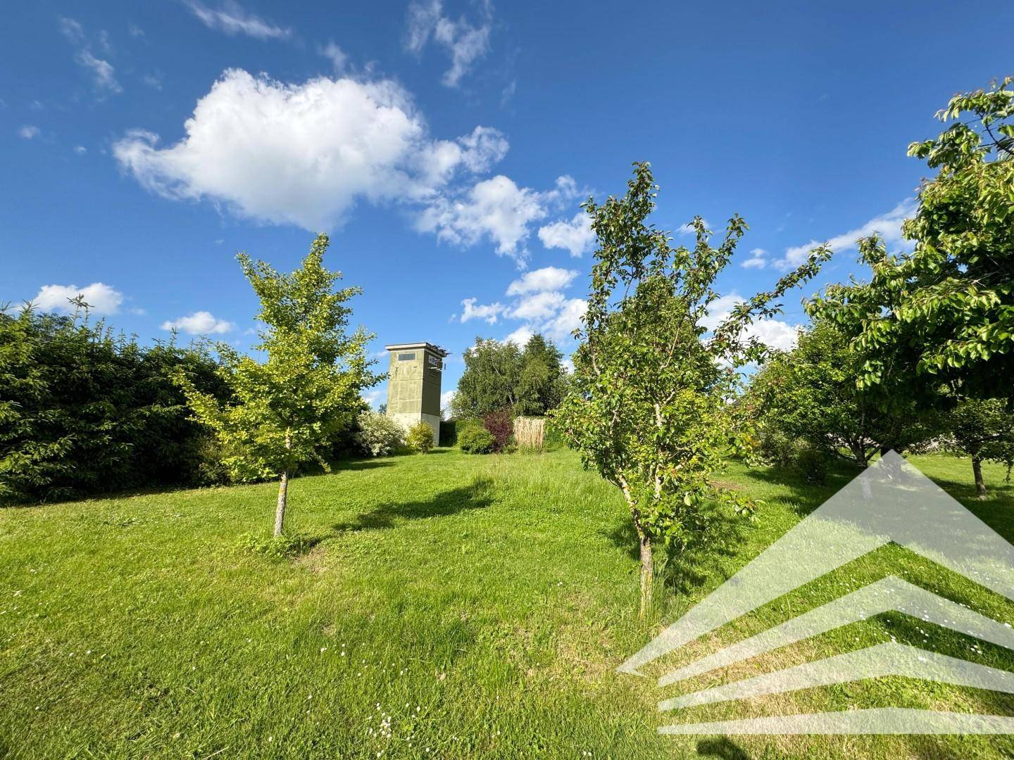 Grüne Gartenfläche mit Bäumen und einem markanten Turm im Hintergrund unter blauem Himmel.