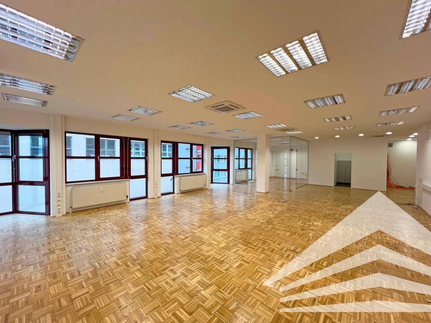 Weitläufiger Bürobereich mit Holzparkett, großen Fenstern und modernen Glasabtrennungen.