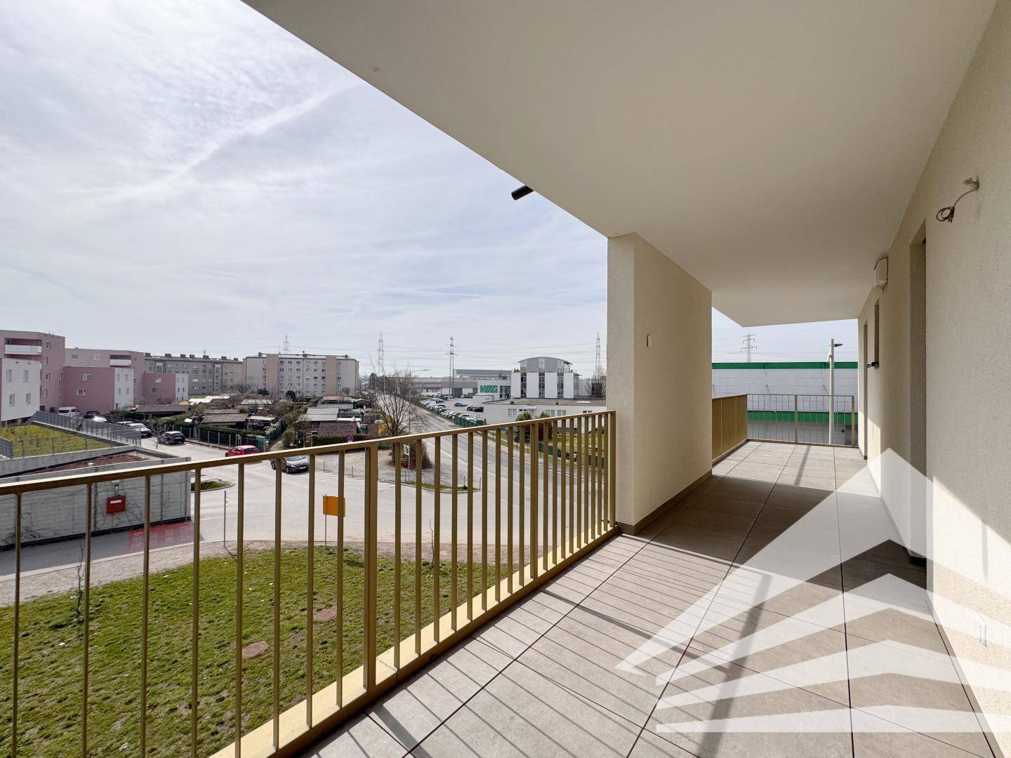 Langer Balkon mit Fliesenboden und Blick auf die Umgebung und andere Gebäude.