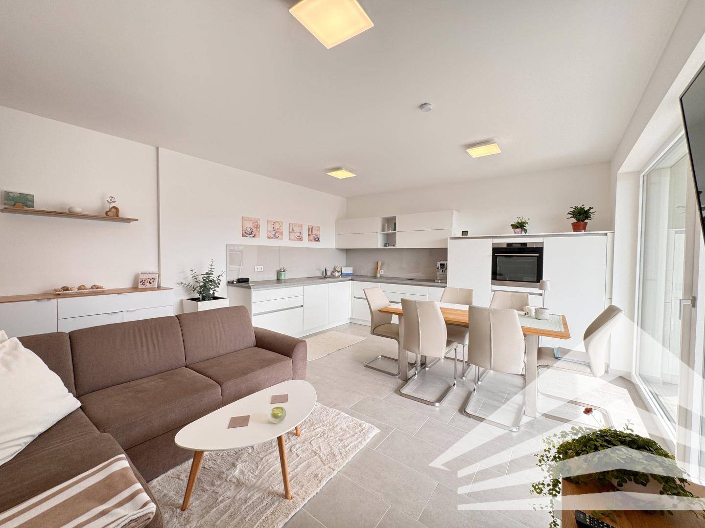 Lichtdurchfluteter Wohn-Essbereich mit integrierter Küche und gemütlichem Sofa.