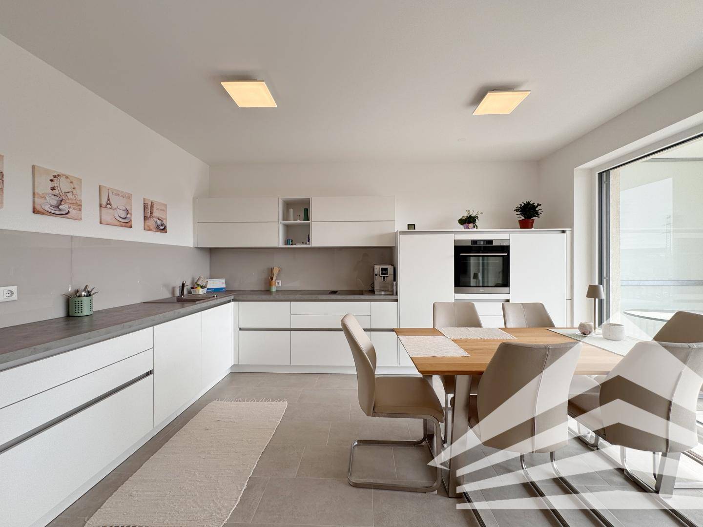 Moderne Einbauküche mit weißen Fronten, grauer Arbeitsplatte und Essbereich.