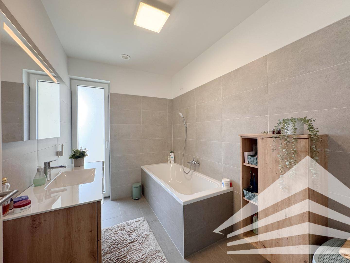 Modernes Badezimmer mit Badewanne, Einzelwaschbecken und großformatigen Fliesen.