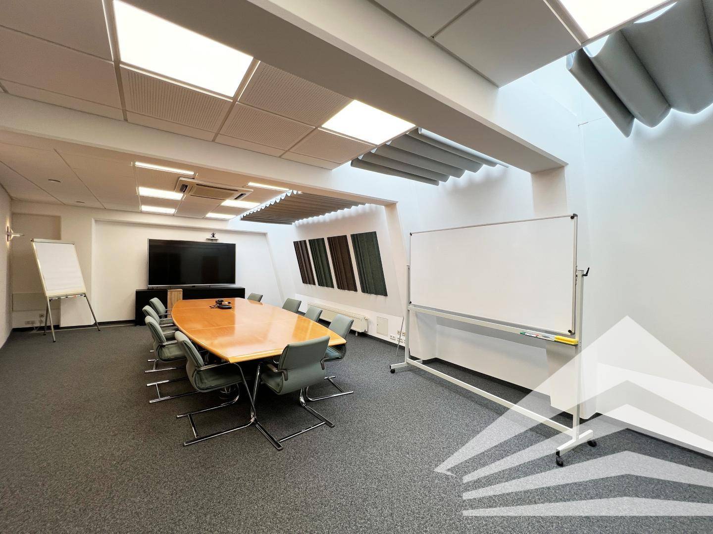 Großer Konferenzraum mit Präsentationstechnik, Whiteboard und akustischen Wandpaneelen für professionelle Meetings.