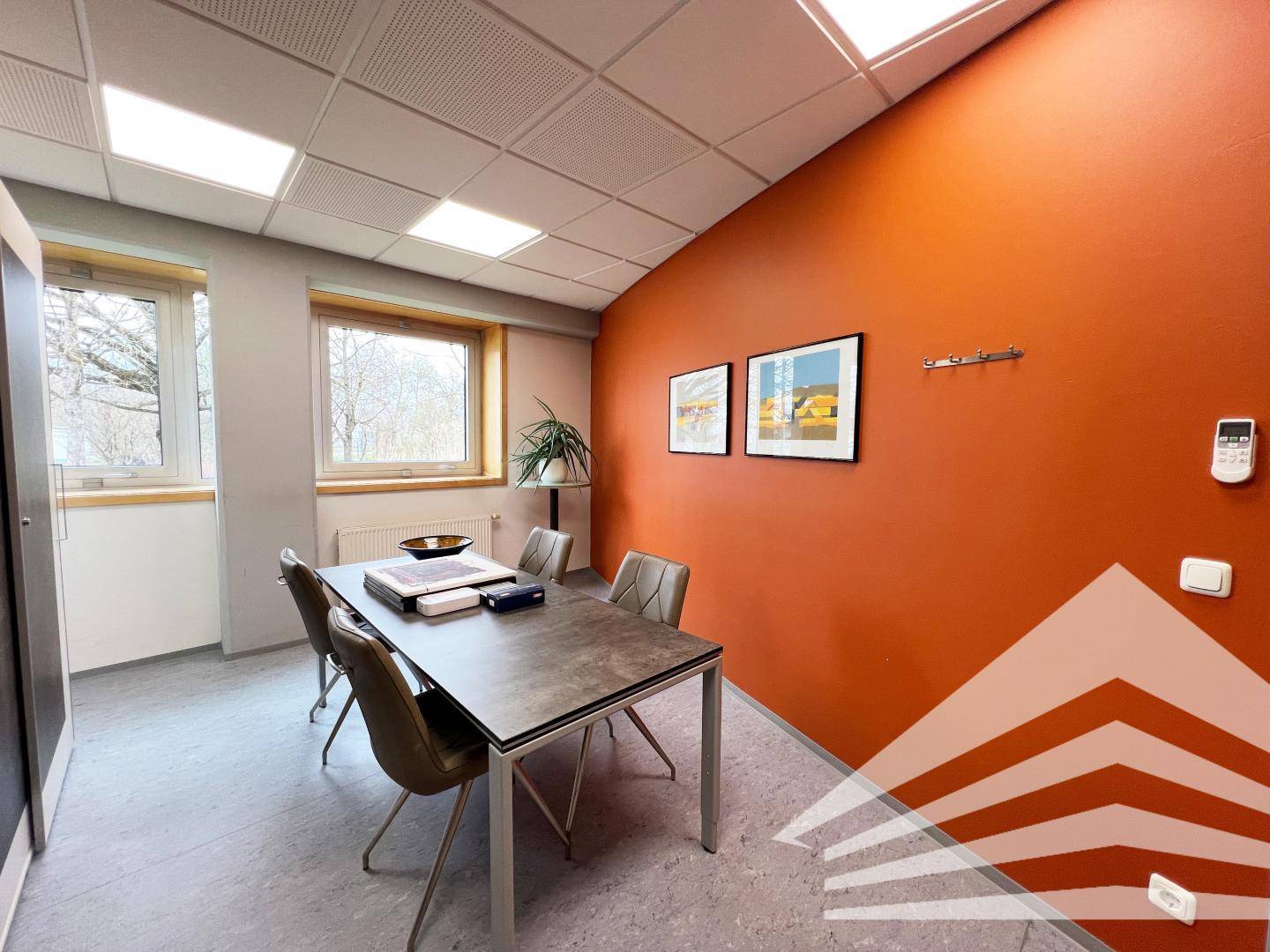 Kleiner Besprechungsraum oder Büro mit orangefarbener Akzentwand, Tisch und Stühlen.