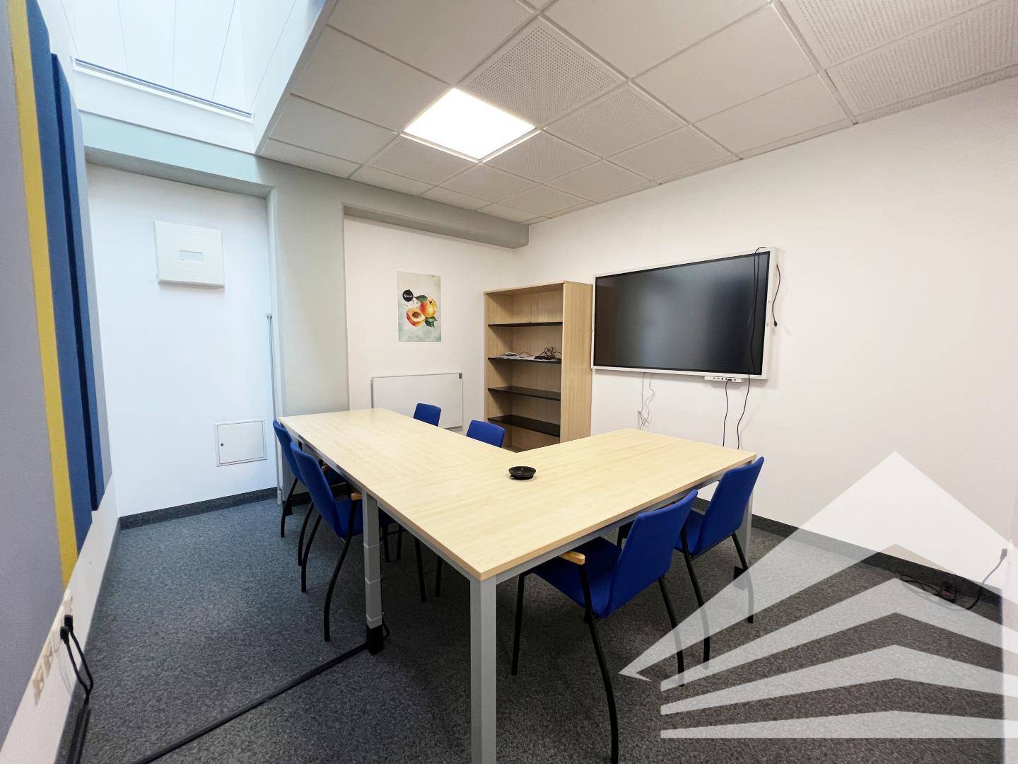 Besprechungsraum mit U-förmigem Tisch, blauen Stühlen und großem Wandbildschirm für Präsentationen.