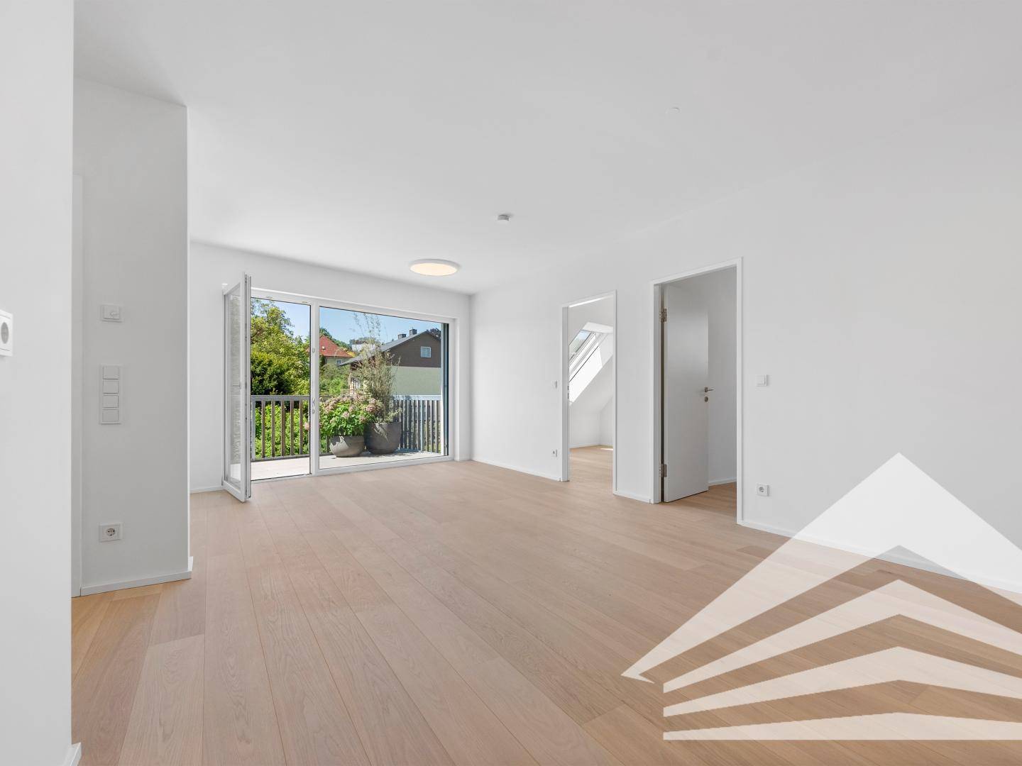 Heller Raum mit Zugang zu einem Balkon, hellem Parkettboden und weißen Wänden.