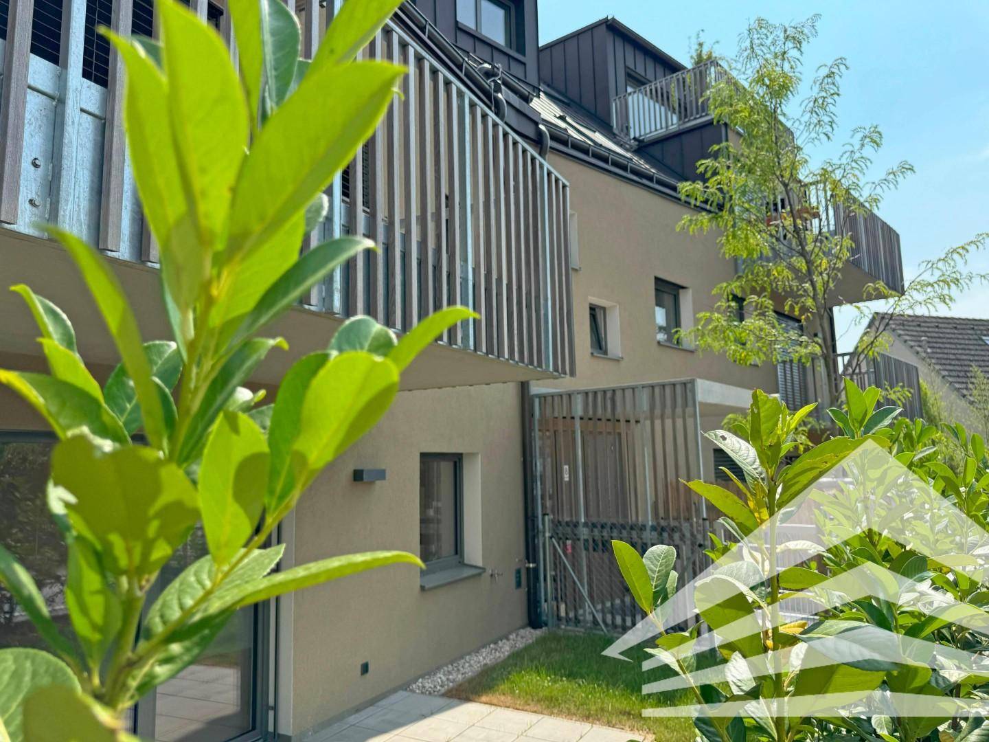 Moderne Gebäudefassade mit Balkonen und einem kleinen, gepflegten Gartenbereich.