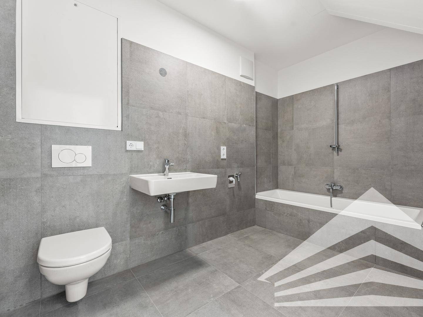 Modernes Badezimmer mit grauen Fliesen, wandhängendem WC und Badewanne mit Duschfunktion.