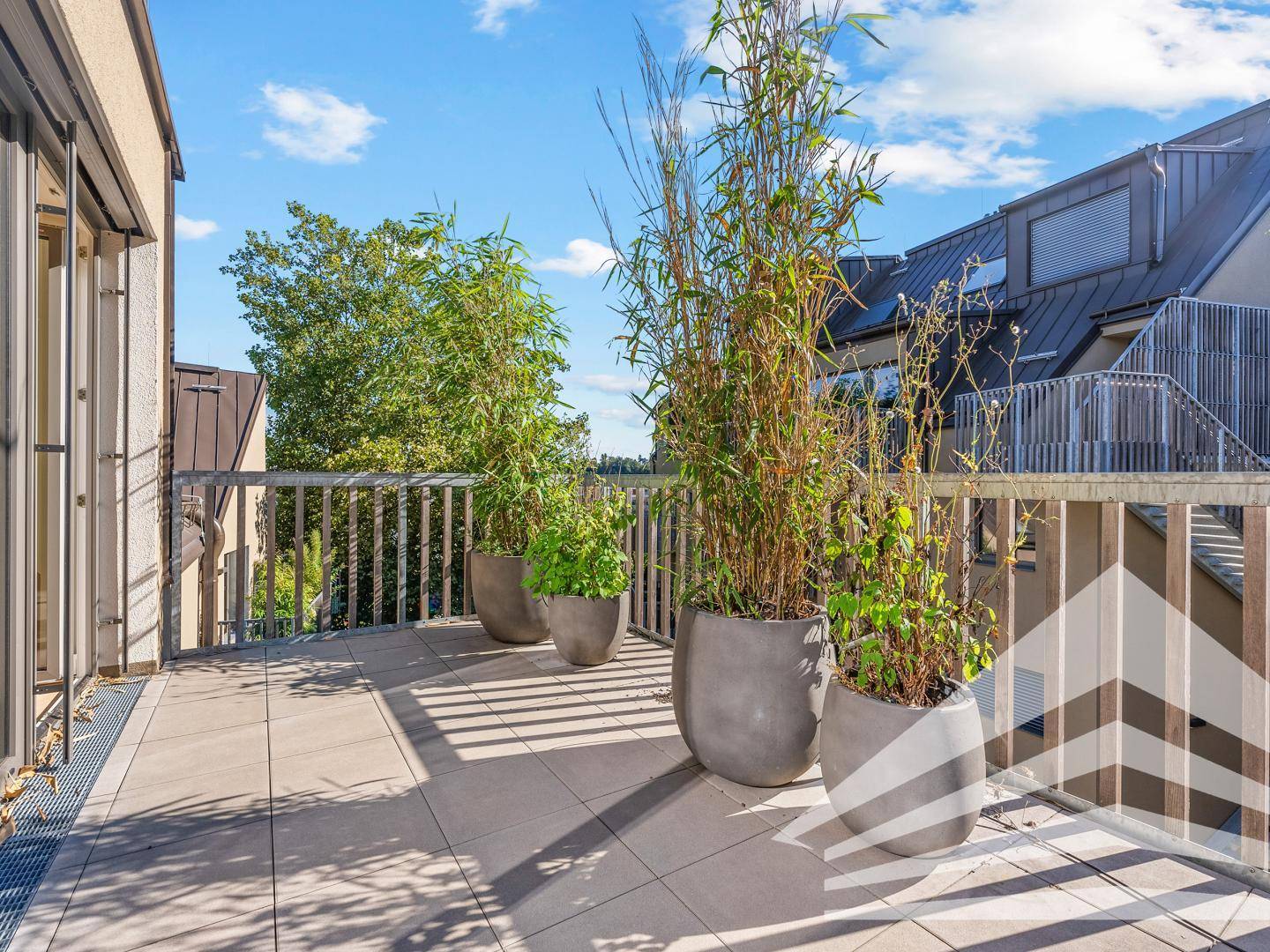 Geräumige Dachterrasse mit Fliesenboden, Pflanzen und Blick auf die Umgebung.