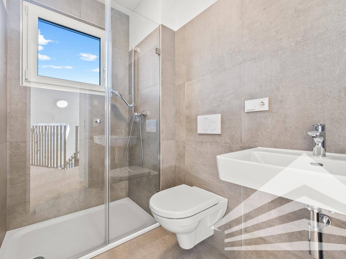 Modernes Badezimmer mit grauen Fliesen, wandhängendem WC und begehbarer Dusche mit Fenster.