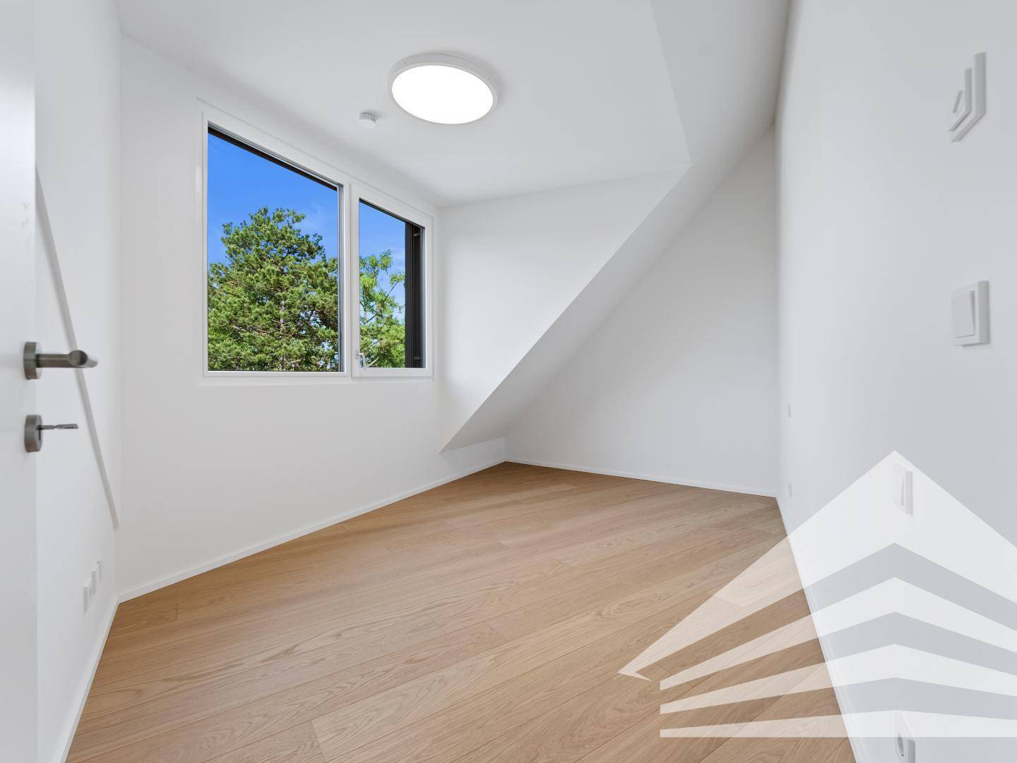 Helles, unmöbliertes Zimmer mit großem Fenster und Holzfußboden, bietet Blick ins Grüne.