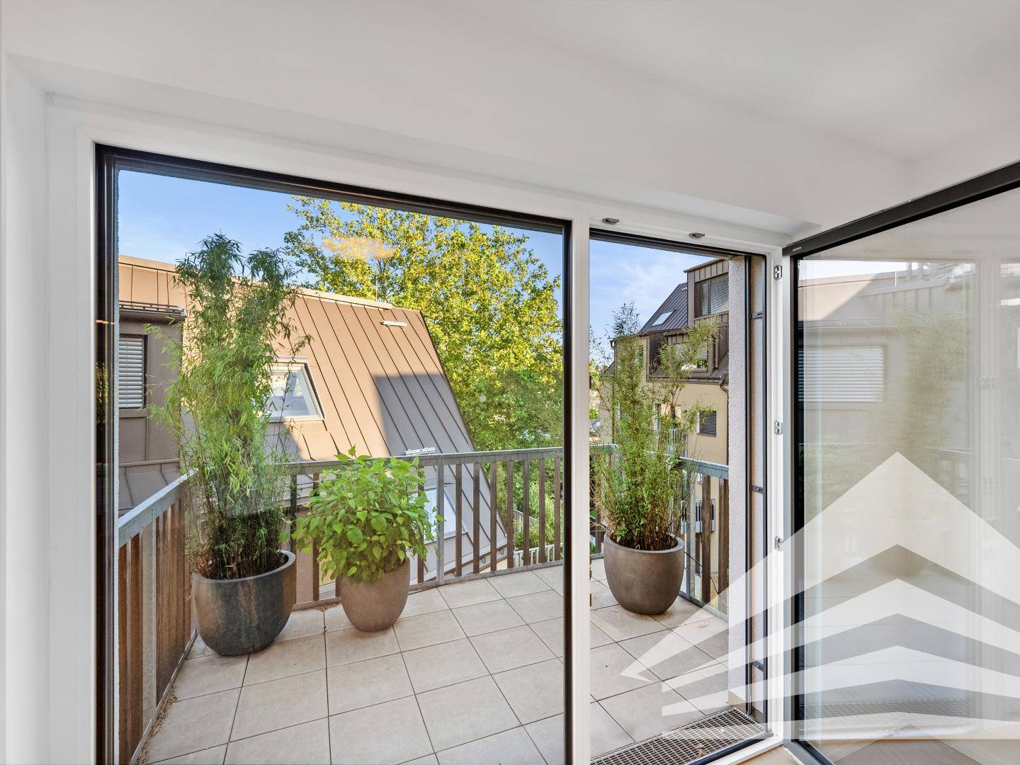 Balkon mit Fliesenboden und Holzgeländer, umgeben von Bäumen und anderen Gebäuden.