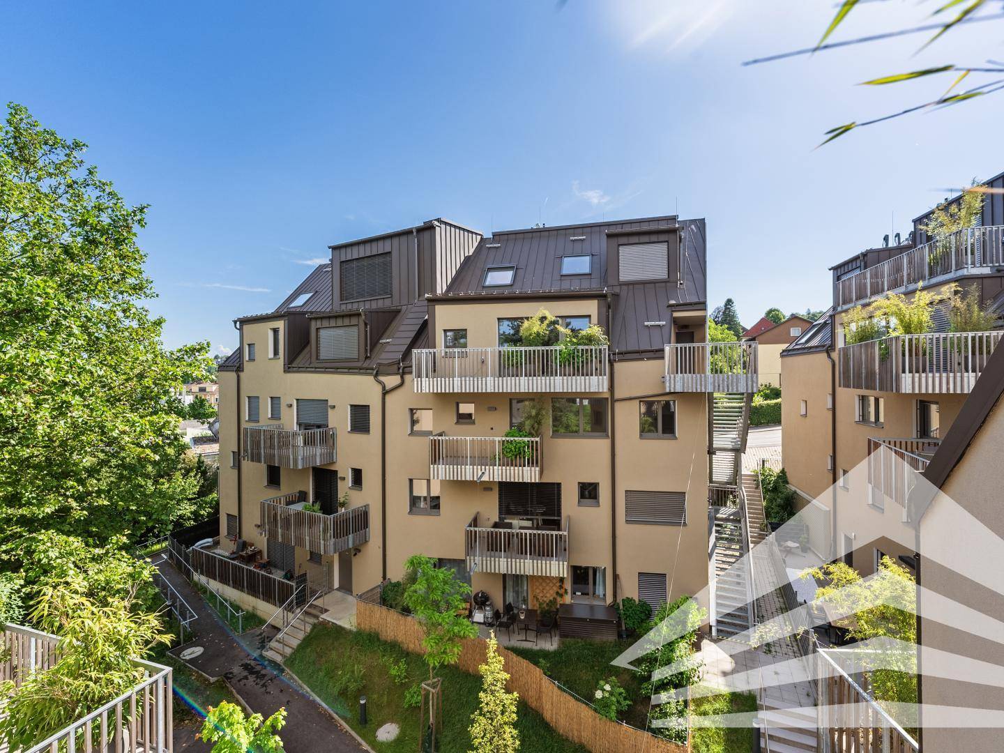 Modernes Mehrfamilienhaus mit mehreren Balkonen und Dachterrassen, umgeben von viel Grün.