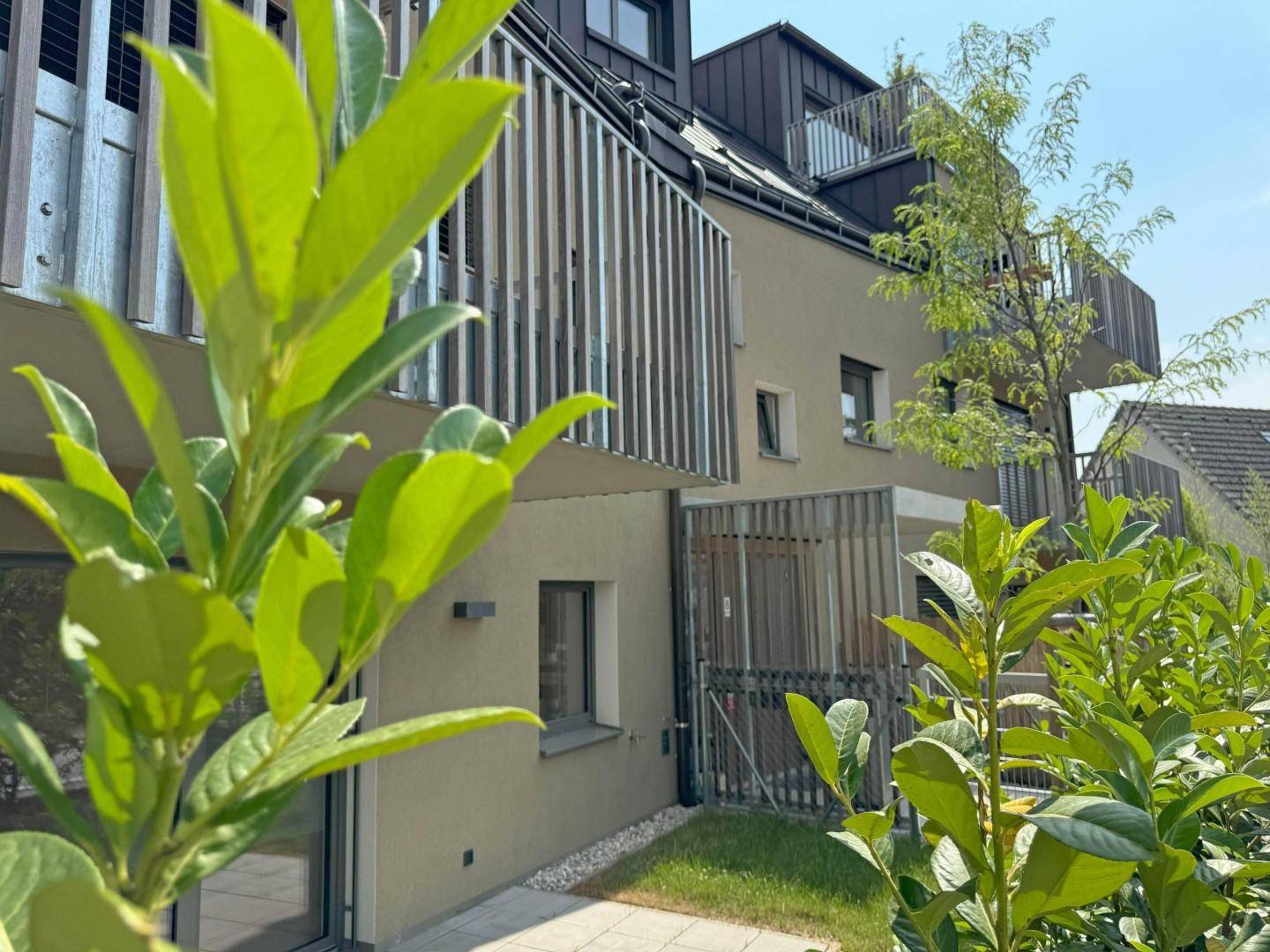 Moderne Gebäudefassade mit Balkonen und üppiger Bepflanzung im Vordergrund.