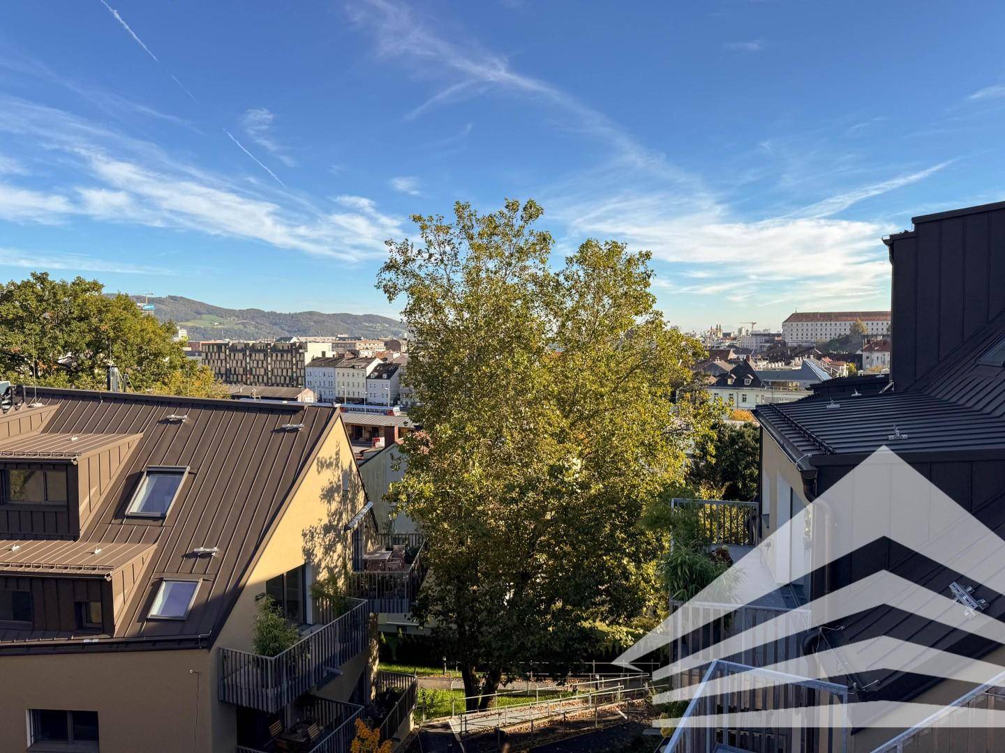 Weitläufiger Blick über die Stadt und grüne Hügel unter blauem Himmel.