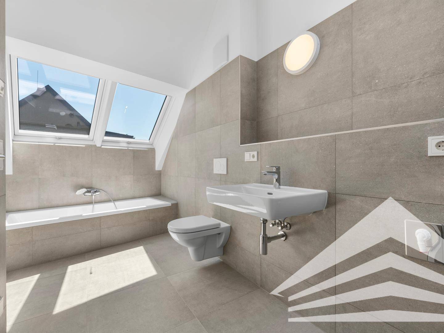 Modernes Badezimmer mit Badewanne, Wand-WC, Waschbecken und Dachfenstern.