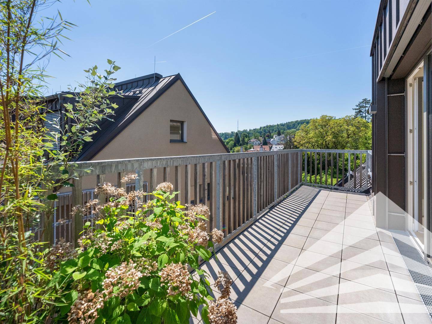 Sonniger Balkon mit Fliesenboden, Metallgeländer und Blick auf die Umgebung.