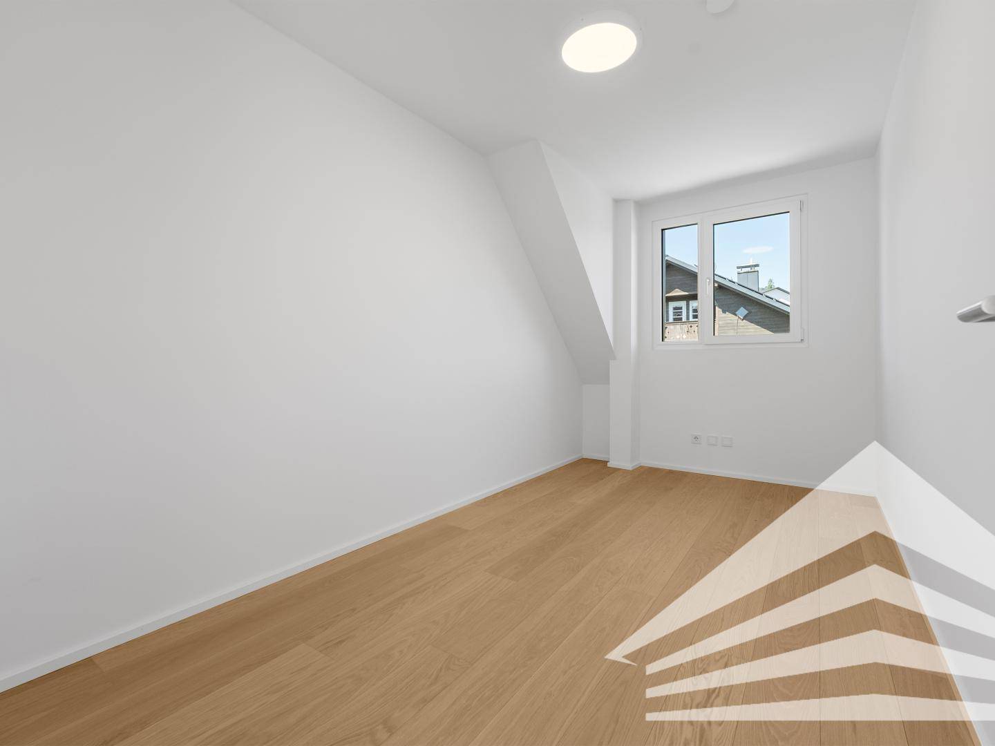 Leeres Zimmer mit Holzboden, weiß gestrichenen Wänden und Fenster mit Ausblick.