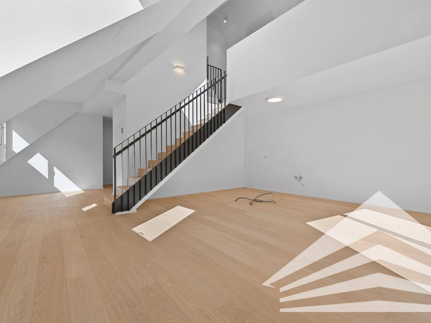 Heller, leerer Wohnbereich mit Holzfußboden, weiß gestrichenen Wänden und moderner Treppe.