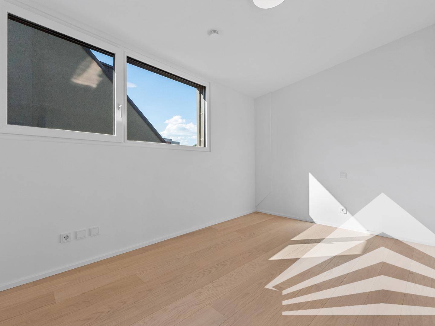 Helles, leeres Zimmer mit Holzboden und großem Fenster, ideal als Schlaf- oder Arbeitszimmer.
