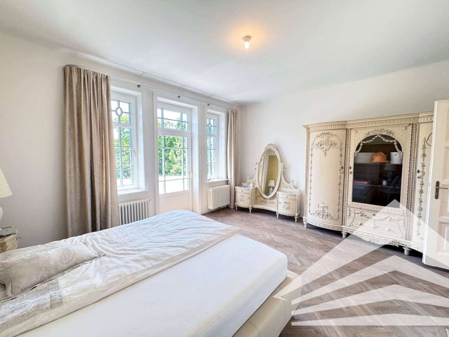 Helles Schlafzimmer mit Parkettboden, großen Fenstern und klassischem Mobiliar.