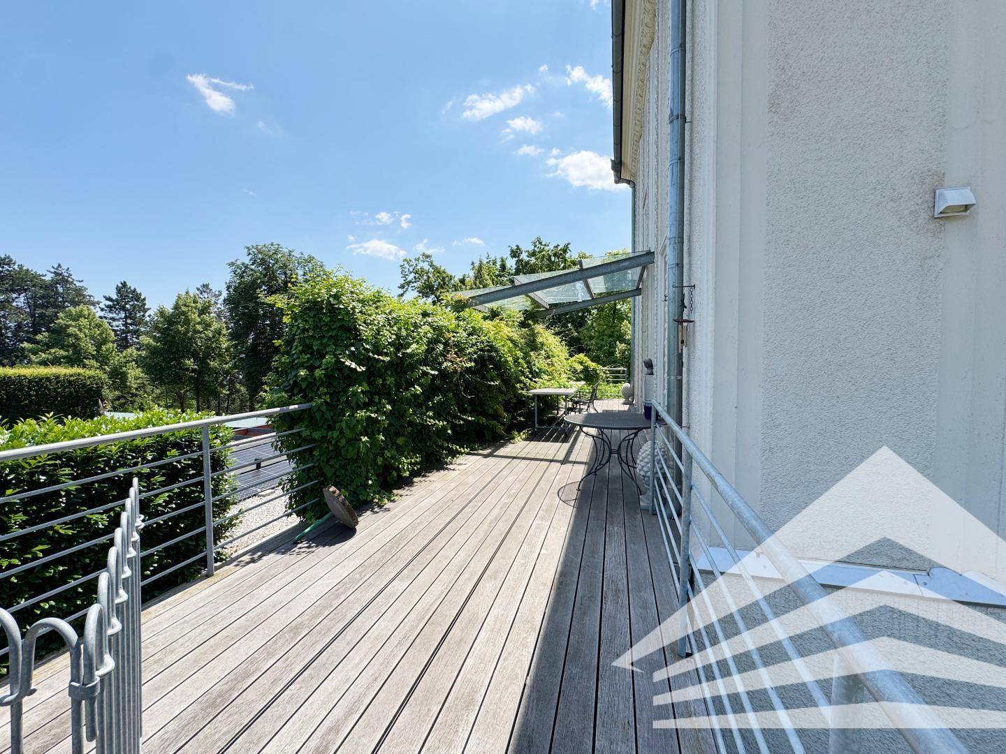 Lange Holzterrasse mit Sitzgelegenheiten und üppiger Bepflanzung.