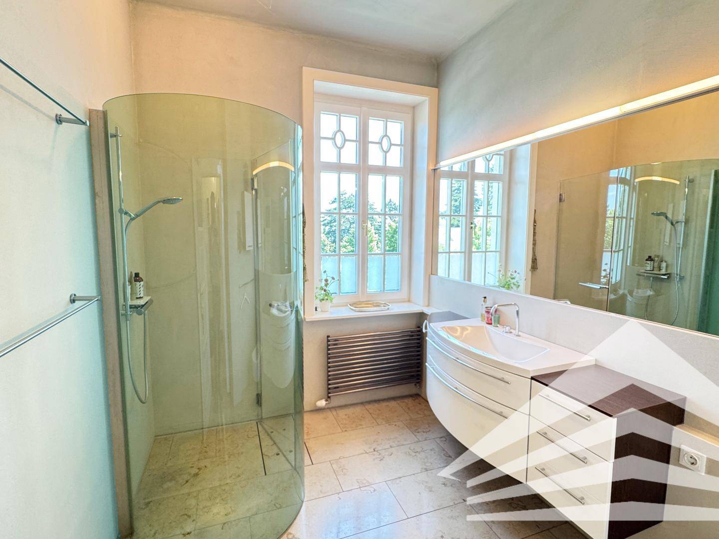 Modernes Badezimmer mit runder Glasdusche, Waschtisch und Fenster.